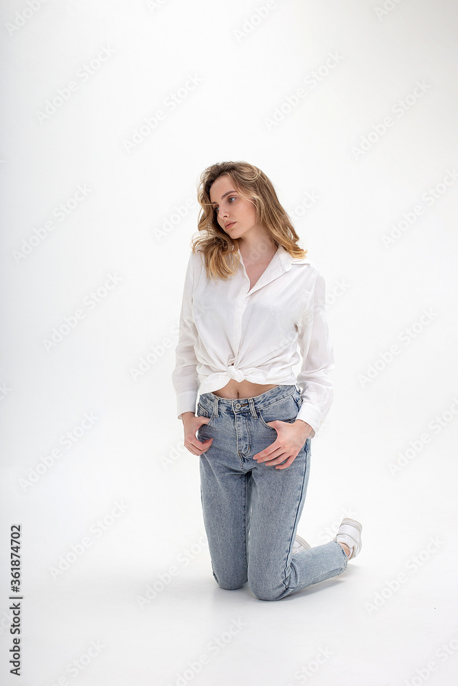 portrait of young pensive caucasian woman posing in shirt and blue jeans,  standing on white studio