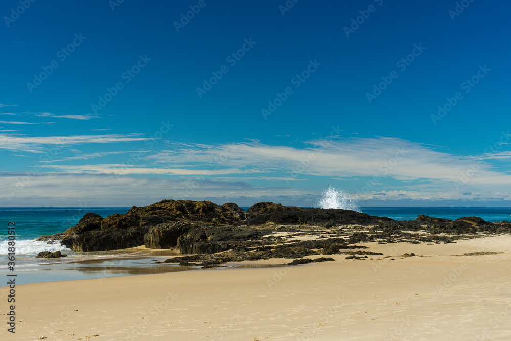 Sandy beach with waves breaking on rocks, blue sky and clouds at Currumbin Beach, Gold Coast, Queensland, Australia.