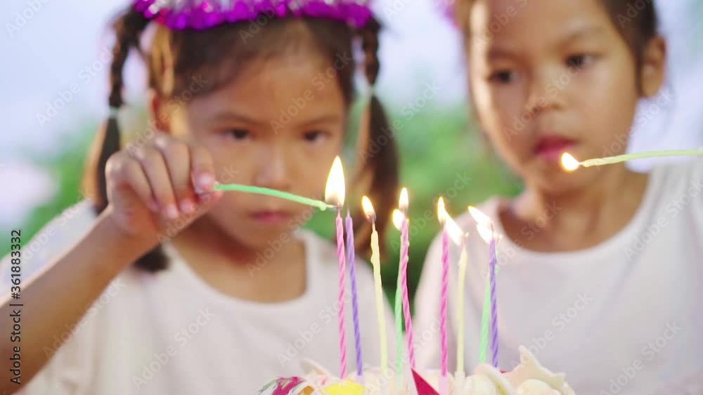 Asian little girls with her sister light the candles on birthday cake at home together. Preparation on birthday party. Slow motion Asian little girls with her sister light the candles on birthday cake at home together. Preparation on birthday party. Slow motion
