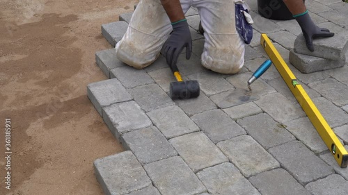 A craftsman lays concrete paving stone blocks on sand. Paving stone work.