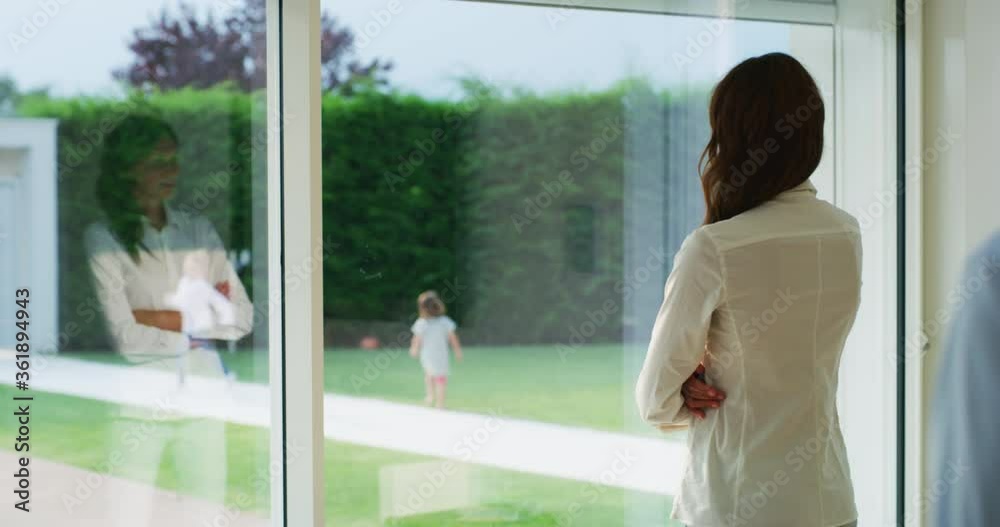 Authentic shot of lovely married couple is enjoying time together while looking through a window and watching their kids playing in a garden at home.
