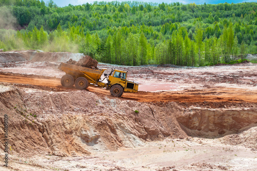 A clay truck is driving through a quarry with red clay. Clay mining.