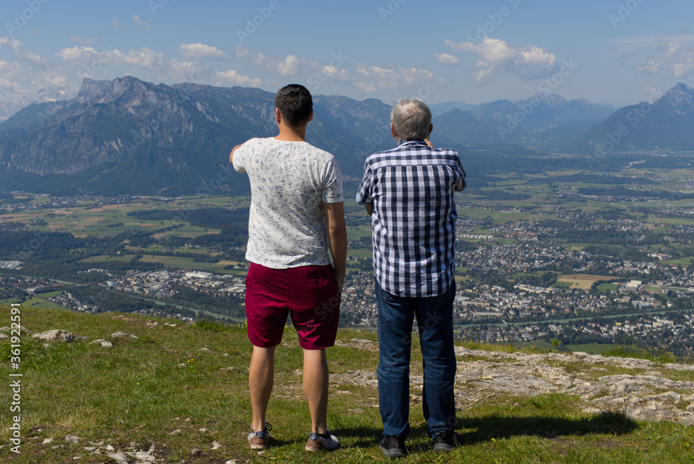 Father and Son standing on top of the mountain covered grass watching the city of Salzburg.
