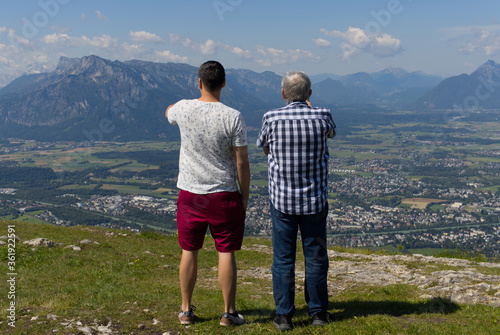 Father and Son standing on top of the mountain covered grass watching the city of Salzburg. © Jacqueline