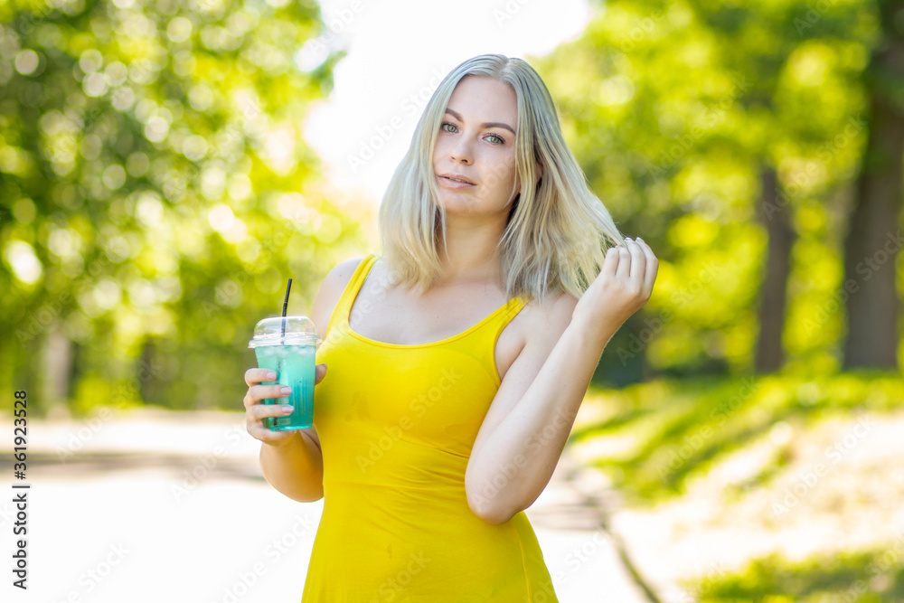 Blonde woman in short yellow dress drinking coctail in park Blonde woman in short yellow dress drinking coctail in park