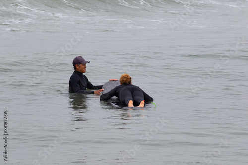 Canvas Print Young multiracial African American lady with amazing smile, freckles & frizzy hair & an Asian Japanese Surf Instructor having a surf lesson together in Chiba, Japan They are wearing black wetsuits