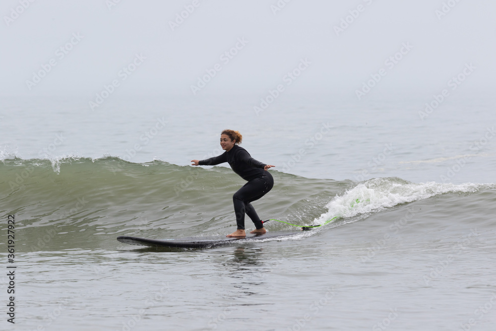 Young multiracial African American lady with amazing smile, freckles & frizzy hair, learning to surf wearing a black wetsuit on a black surfboard. She is Surfing in Chiba Japan near to Ichinomiya. Young multiracial African American lady with amazing smile, freckles & frizzy hair, learning to surf wearing a black wetsuit on a black surfboard. She is Surfing in Chiba Japan near to Ichinomiya.
