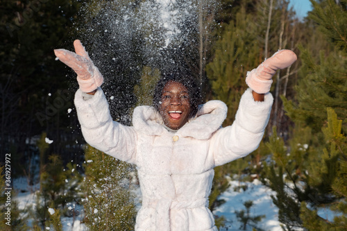 Beautiful dark-skinned woman throws snow on a background of young pines.