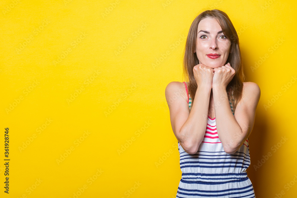 Young woman smiling with fists holds her chin on a yellow background Young woman smiling with fists holds her chin on a yellow background