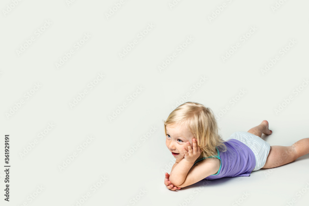 Beautiful cute little baby smiling while lying on her stomach, doing gymnastics on a white background Beautiful cute little baby smiling while lying on her stomach, doing gymnastics on a white background
