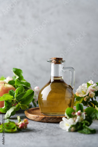 Bottle of apple cider vinegar surrounded by apples and blossoming branches