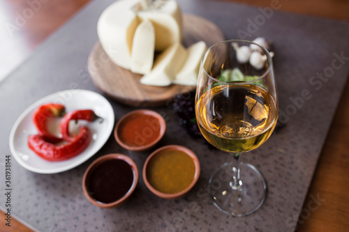 A glass of white wine close-up. Cheese and vegetables are sliced ​​on a board in the background. Georgian cuisine