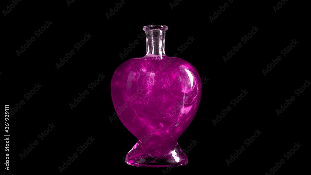 Glass bottle in the form of a heart with pink liquid. The elixir is spinning and overflowing with liquid. Potion of love is isolated on a black background.