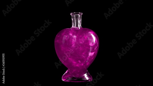 Glass bottle in the form of a heart with pink liquid. The elixir is spinning and overflowing with liquid. Potion of love is isolated on a black background.