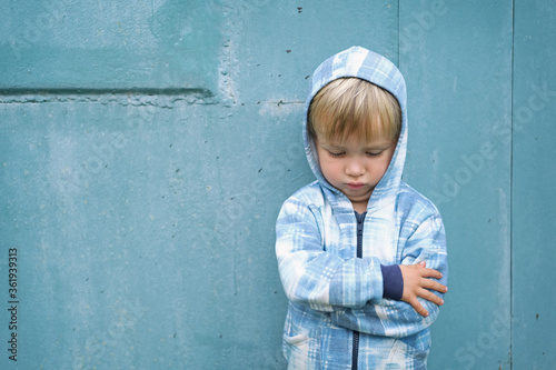 Фотография Sad bored resentful child boy in hoodie standing near blue wall