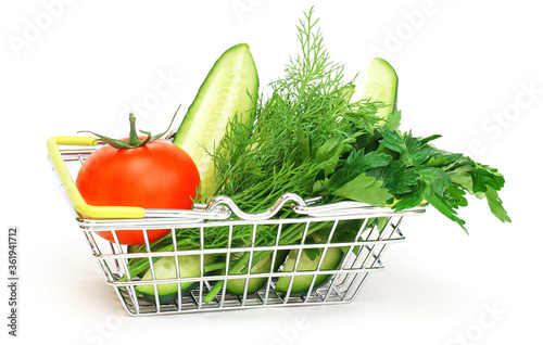 a small shopping basket with herbs, cucumber, tomato, parsley next to a fresh potted green salad on a white background. Healthy food, vegetarian food, vegetables, shopping at the supermarket.