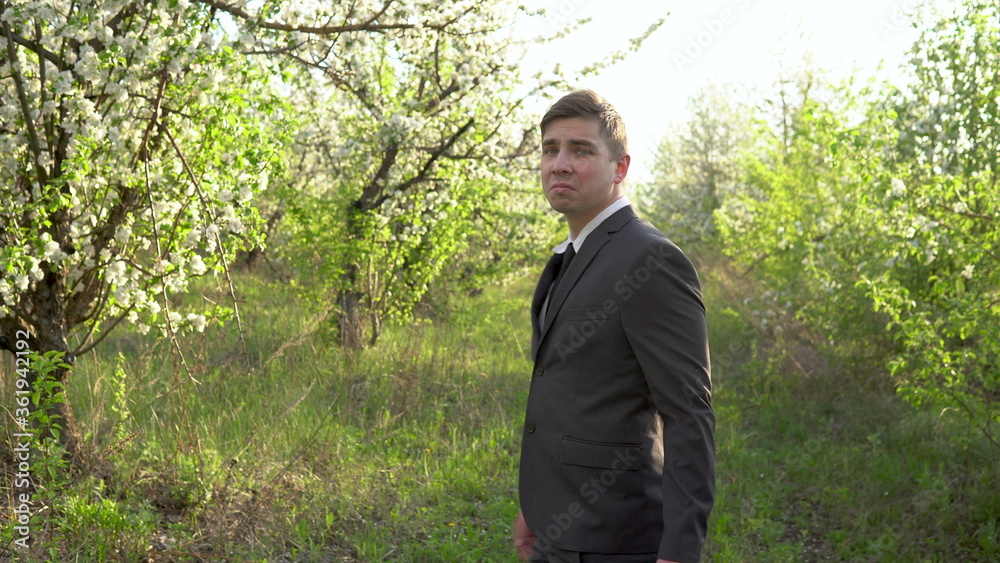 A businessman walks through the apple orchard and looks around. A man in a suit looks at his possessions. A man in nature.