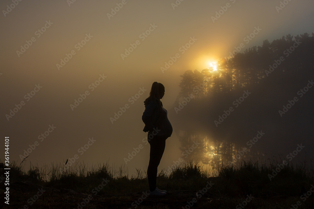 Pregnant woman touch her belly, silhouette photo, beautiful sunrise in the background.