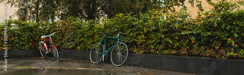 Panoramic shot of bicycles near bushes on urban street