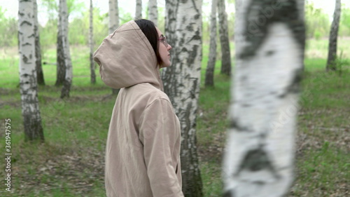 A young woman walks through a birch forest. A girl walks in the park. View through the trees.