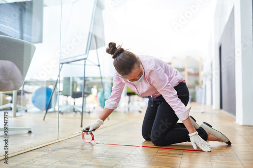 Geschäftsfrau markiert Boden im Büro mit Klebeband © Robert Kneschke