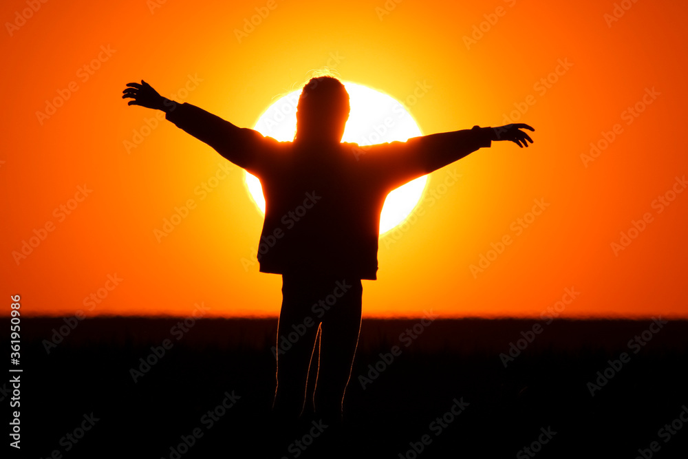 A little girl stands on the meadow and watches the beautiful sunset with her hands outstretched. close up of the sun in the big orange sky.