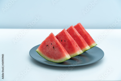 Several pieces of watermelon are placed in a dark blue porcelain dish. A plate of watermelon on a white desktop