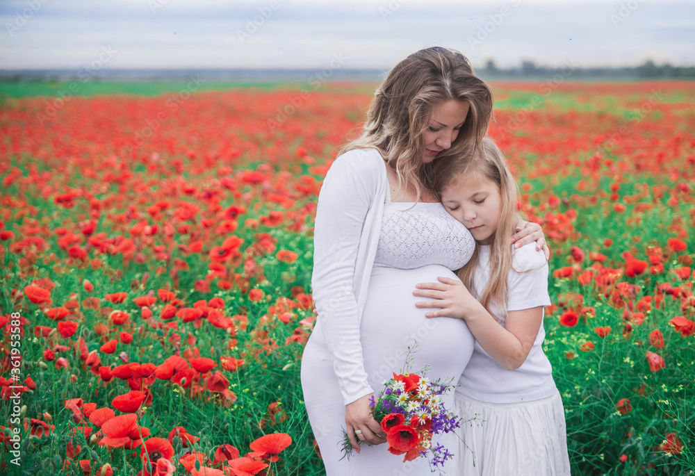 pregnant mother with her eldest daughter dressed in white dresses is cuddle in the middle of a field with red flowers