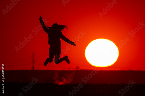 Young woman jumps high and shows the silhouette at sunset.