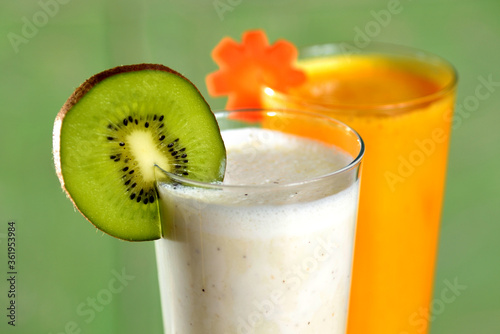 Two smoothie cocktails (fruit of kiwi and vegetable of carrot) on green background