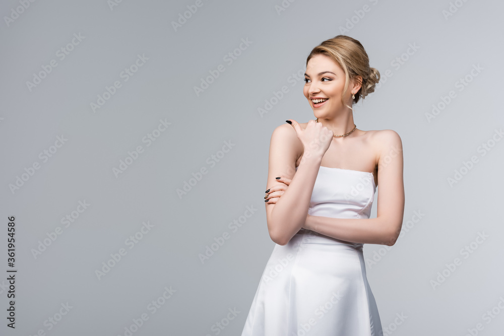 cheerful bride in white wedding dress pointing with thumb and looking away isolated on grey cheerful bride in white wedding dress pointing with thumb and looking away isolated on grey