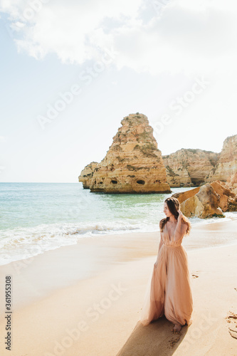 Young female on beach wearing elegant dress. Beautiful Summer Woman on the Beach