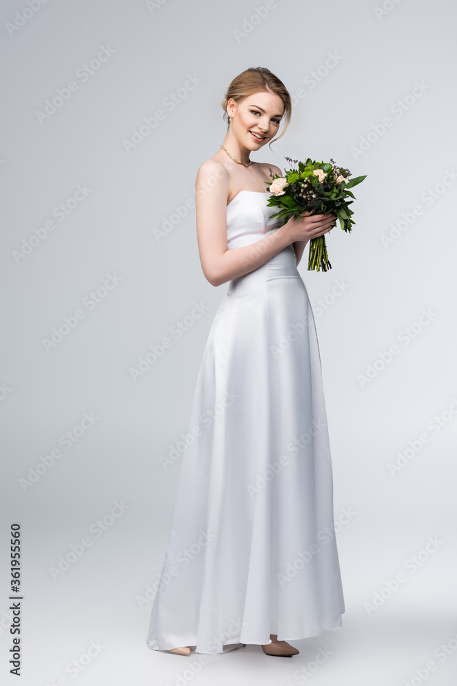 happy bride in white wedding dress holding bouquet of flowers on grey happy bride in white wedding dress holding bouquet of flowers on grey