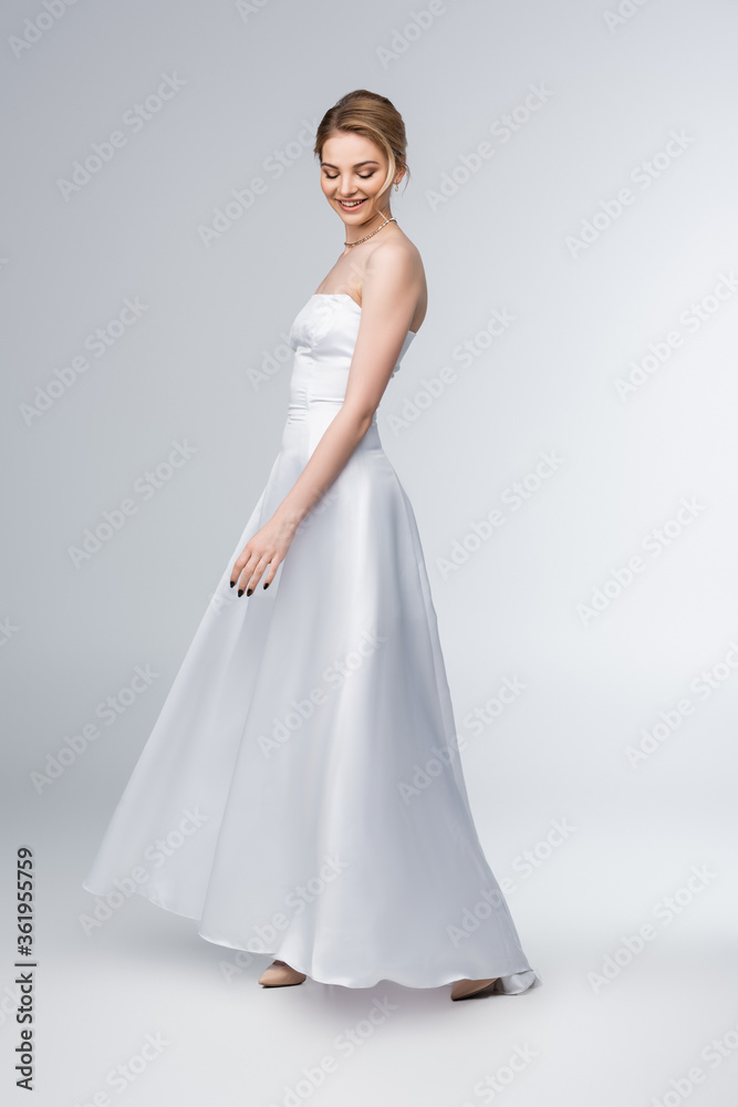 smiling bride in elegant wedding dress standing on grey smiling bride in elegant wedding dress standing on grey