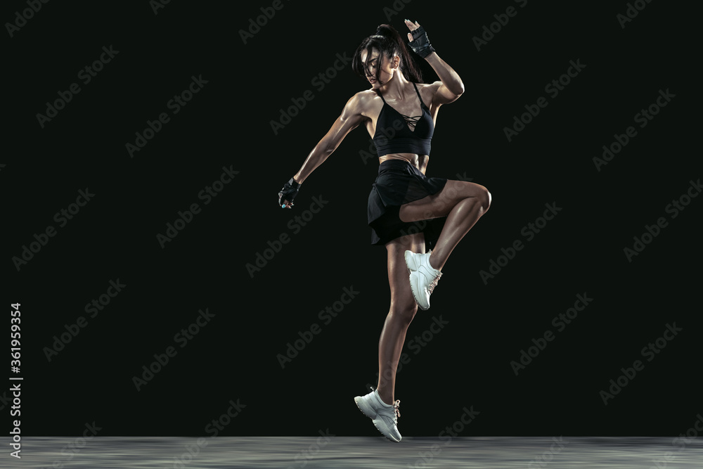 Beautiful young female athlete practicing on black studio background, full length portrait. Sportive fit brunette model in run, jump. Body building, healthy lifestyle, beauty and action concept.