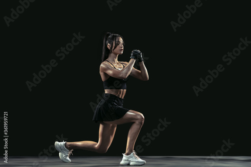 Beautiful young female athlete practicing on black studio background, full length portrait. Sportive fit brunette model doing sit ups. Body building, healthy lifestyle, beauty and action concept.