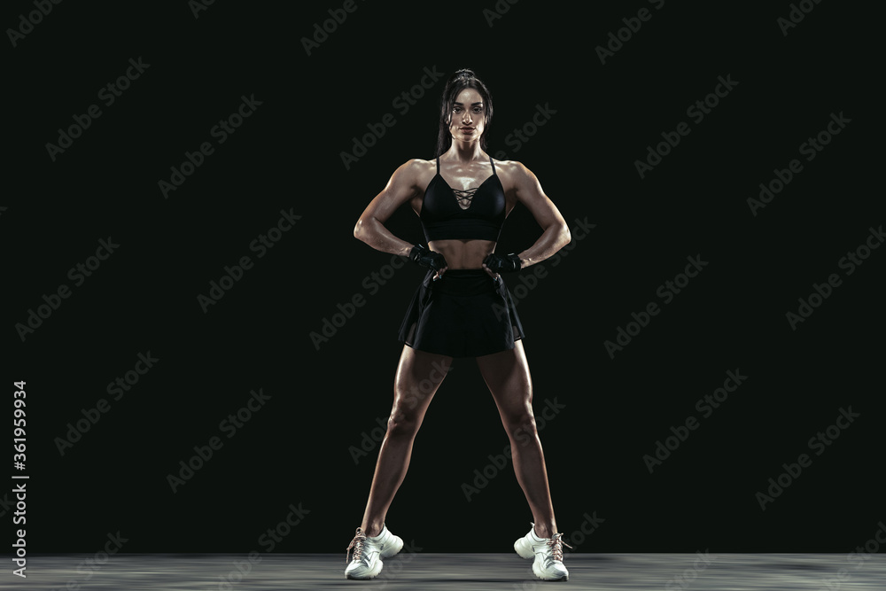 Beautiful young female athlete practicing on black studio background, full length portrait. Sportive fit brunette model posing confident. Body building, healthy lifestyle, beauty and action concept.