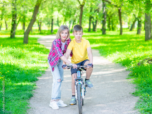 Happy family. Sporty family leisure. Mom teaches her young son ride a bike in summer park. Empty space for text © Ermolaev Alexandr