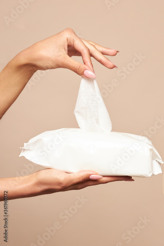 Hygiene. Female hands takes wet wipes from white packaging on a beige background. Daily hygiene for the prevention of viral and bacterial infections.