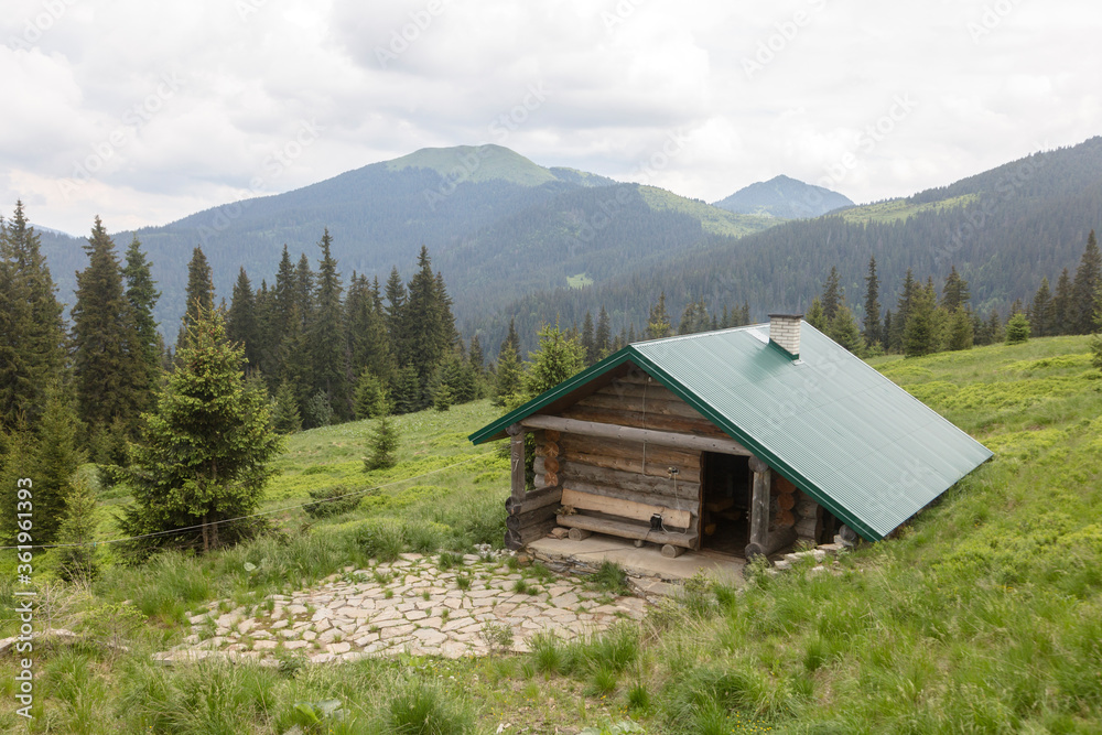 Mountain hut on a green meadow with spruce forest. Mount Berlebashka, Carpathians, Marmaroshchyna, Maramures, Ukraine