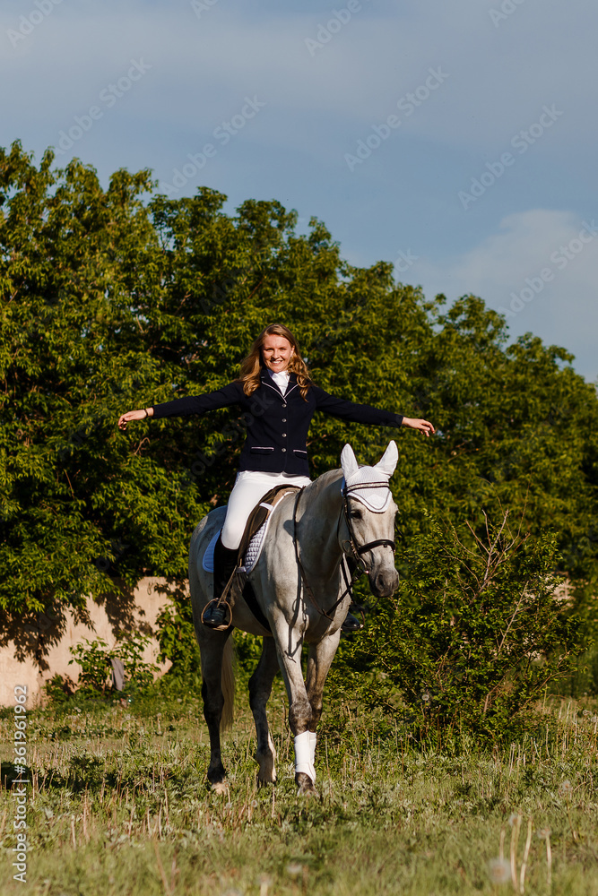 Teenage girl jumps on white horse raising hands to side