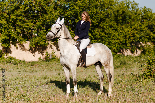 Teenage girl sits on a beautiful white horse.