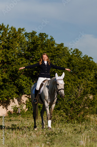 Teenage girl jumps on white horse raising hands to side © Alyona