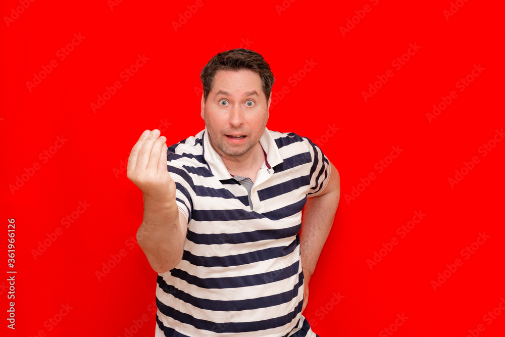 confusion man wearing horizontal striped t-shirt standing over red background doing money gesture with hands. confusion man wearing horizontal striped t-shirt standing over red background doing money gesture with hands.