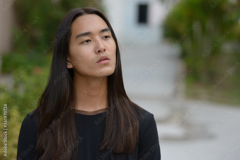 Face of young Asian man with long hair thinking at the park