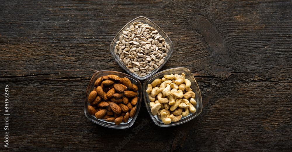 Almond, sunflower seeds and cashew in a small plates which standing on a vintage wooden table. Nuts is a healthy vegetarian protein and nutritious food.