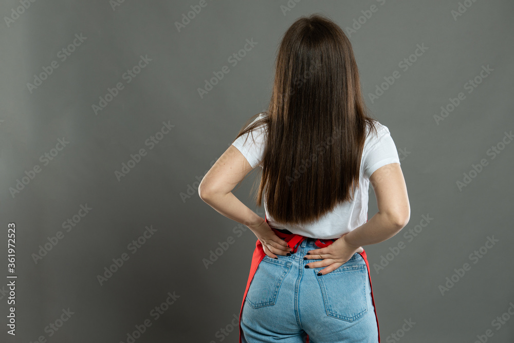 Back view of female supermarket employee holding lower back like hurting