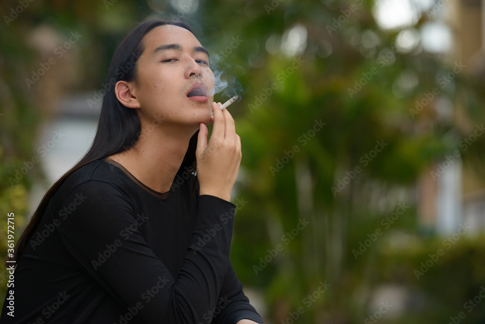 Young Asian man with long hair smoking at the park Young Asian man with long hair smoking at the park