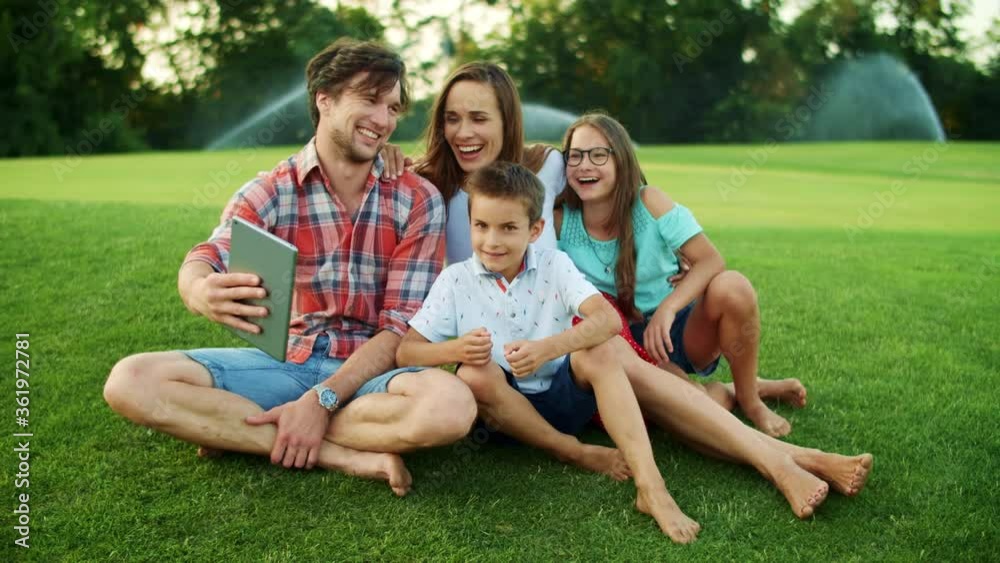 Family laughing together in park. Family having video chat on pad in meadow Family laughing together in park. Family having video chat on pad in meadow