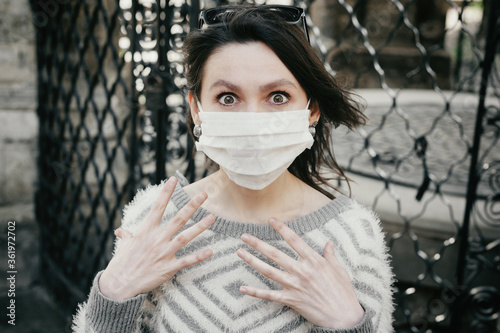 Cuadro en lienzo Shocked brunette woman in medical disposable mask looking at camera